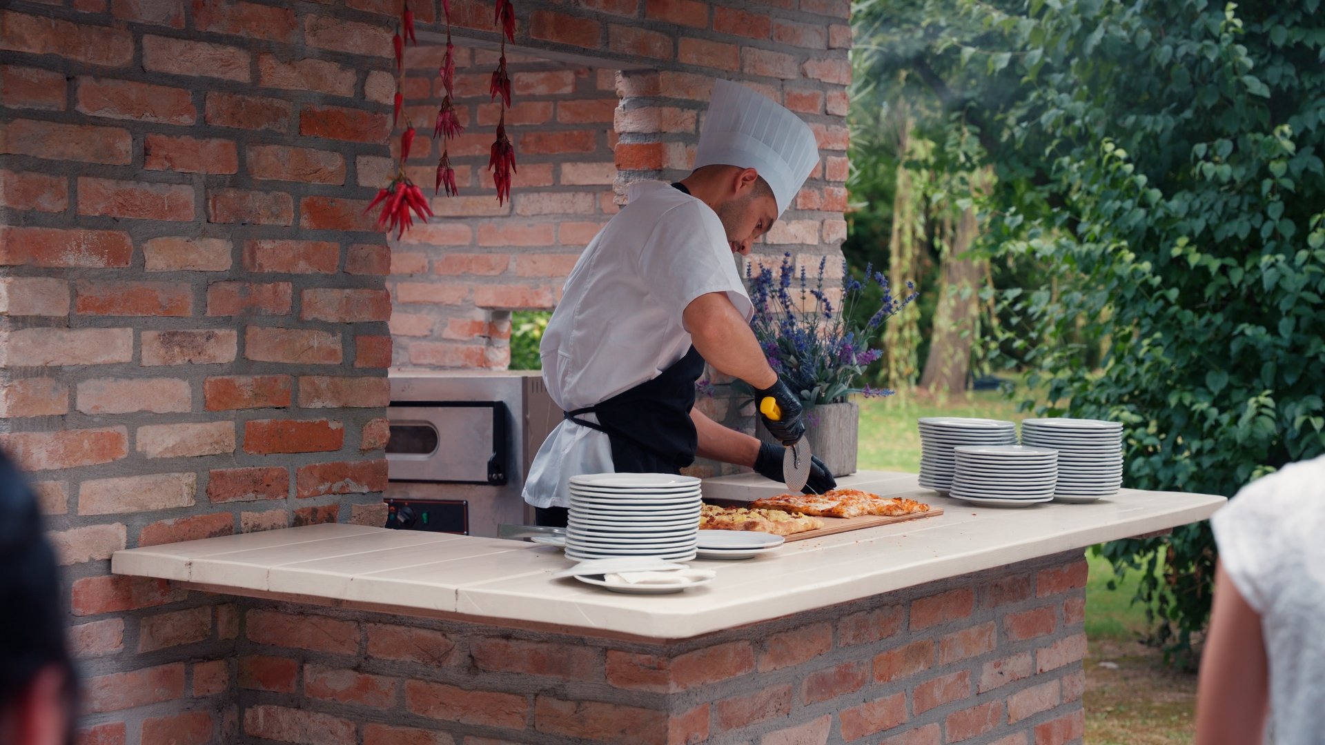 A chef cutting pizza in an outdoor brick kitchen, ungraded flat footage