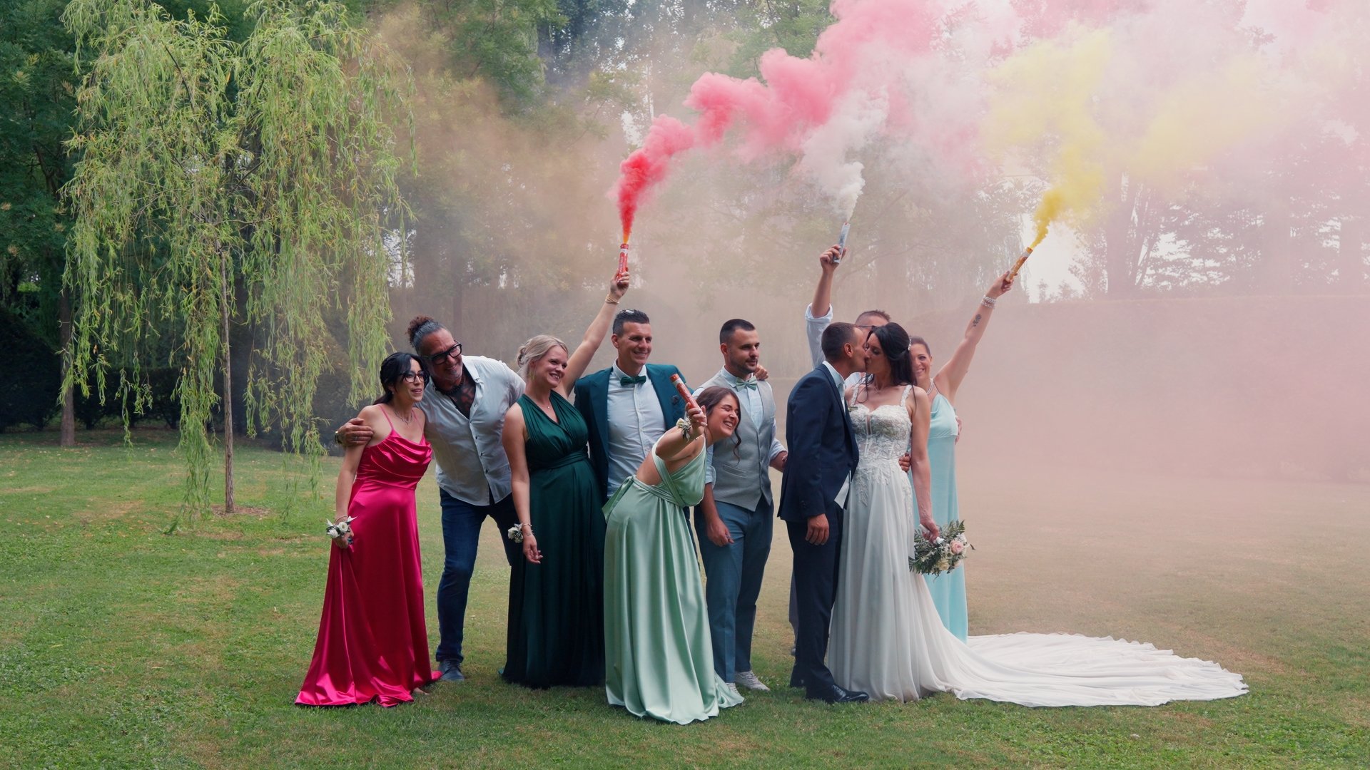 A wedding group with coloured smoke bombs on a lawn, ungraded flat footage